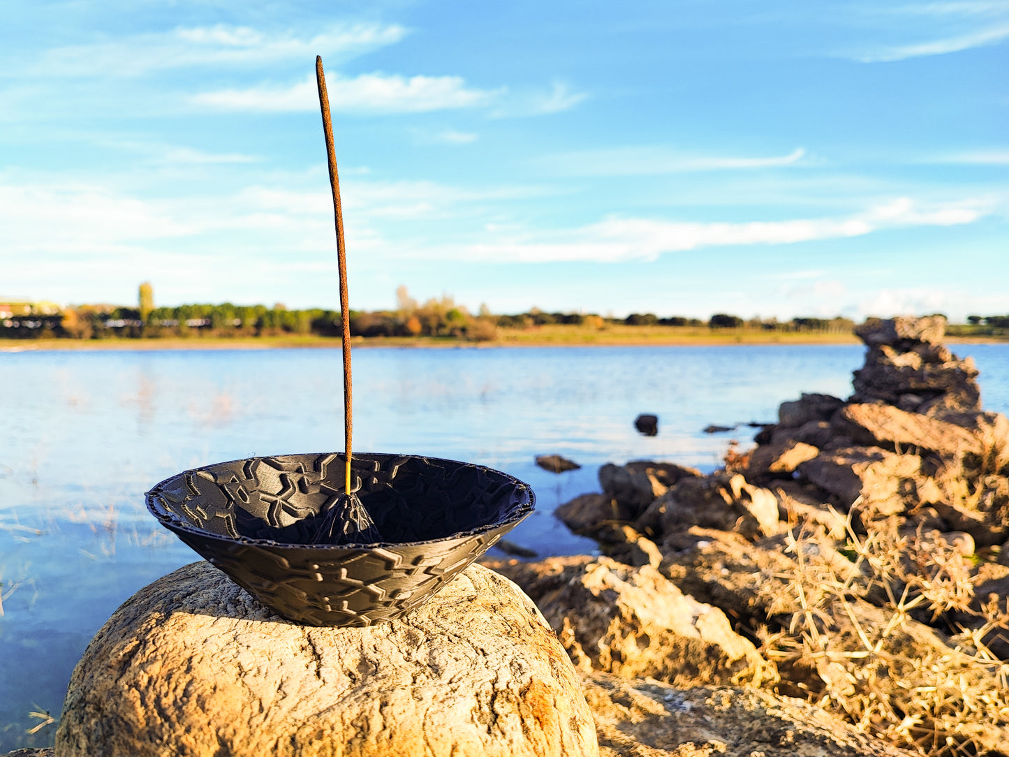 a black bowl sitting on top of a rock next to a body of water