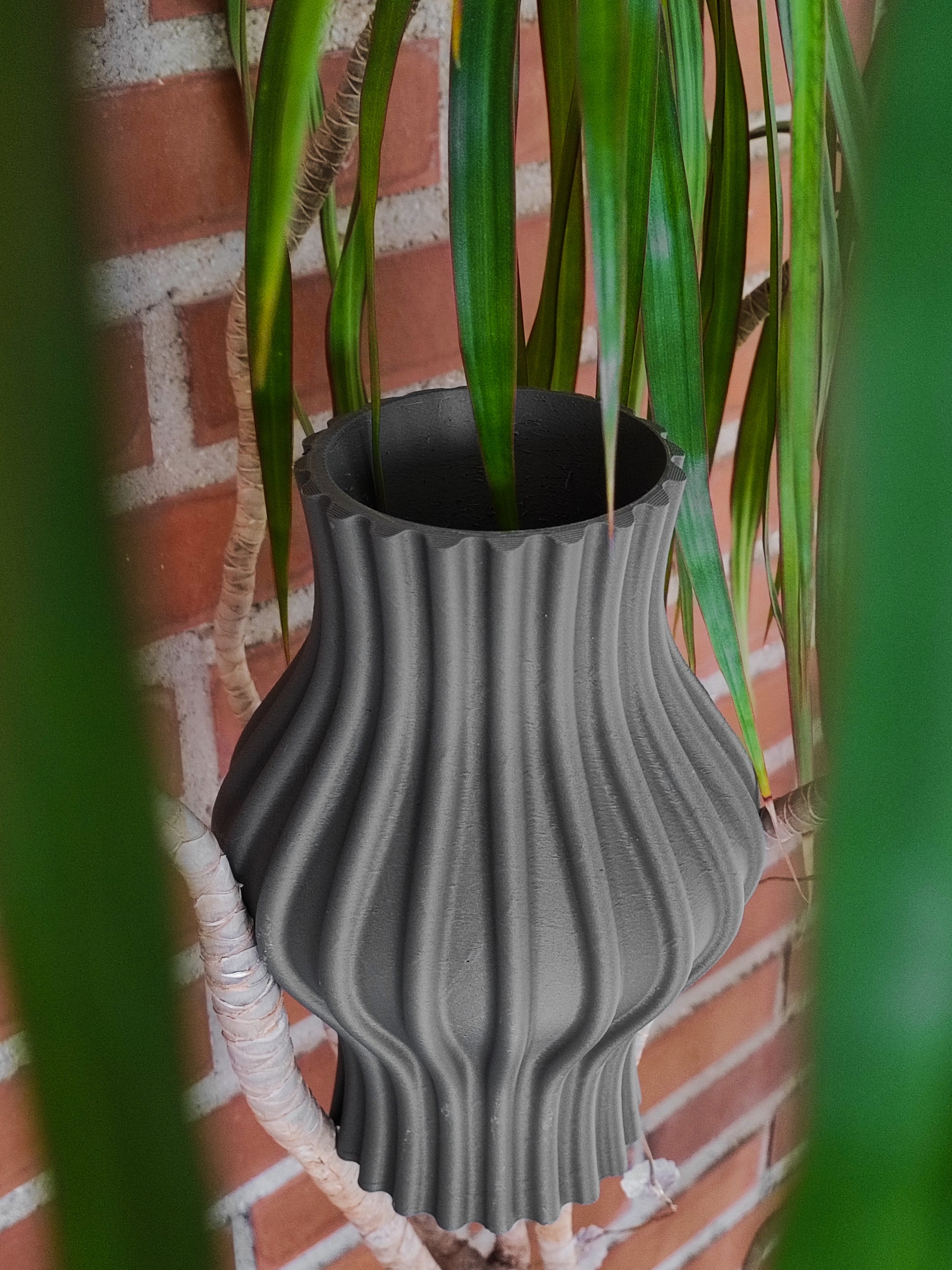 a plant in a gray vase on a brick wall