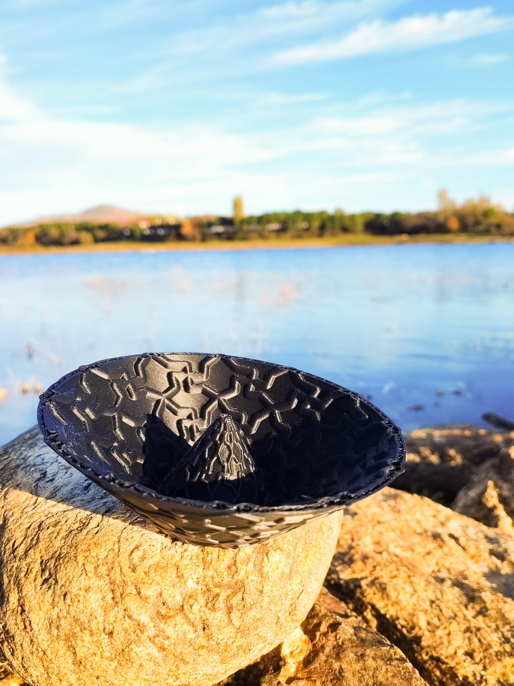 a black bowl sitting on top of a rock next to a body of water