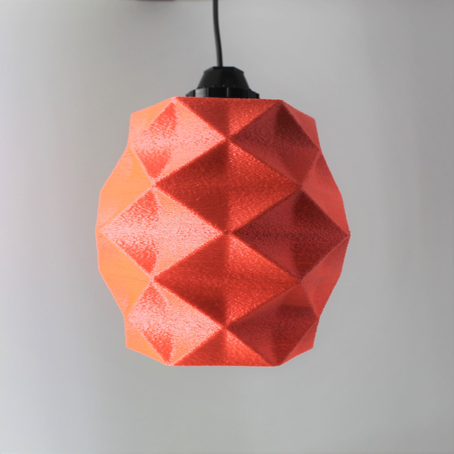 a red origami light hanging from a black cord