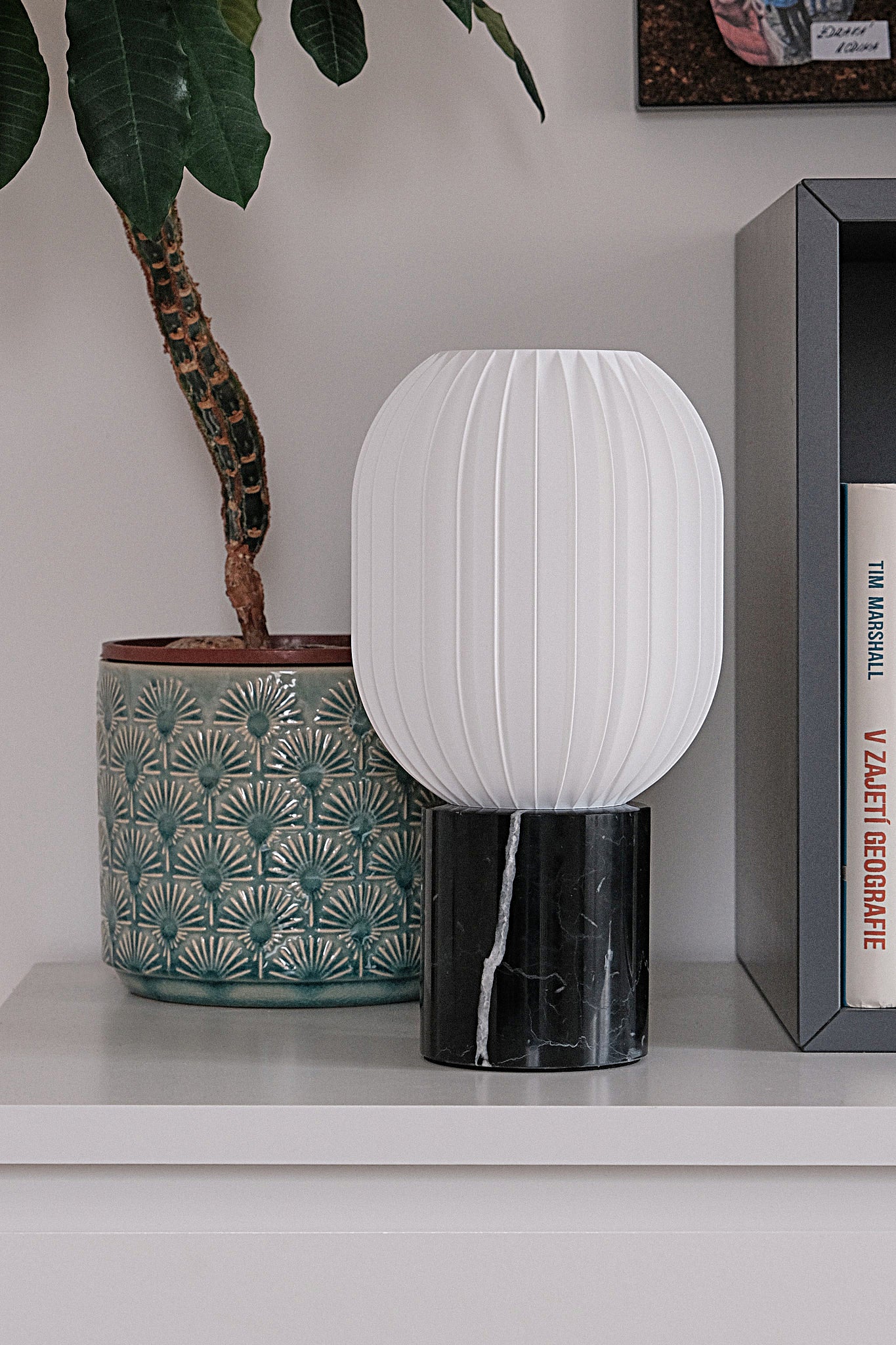 a white lamp sitting on top of a shelf next to a potted plant