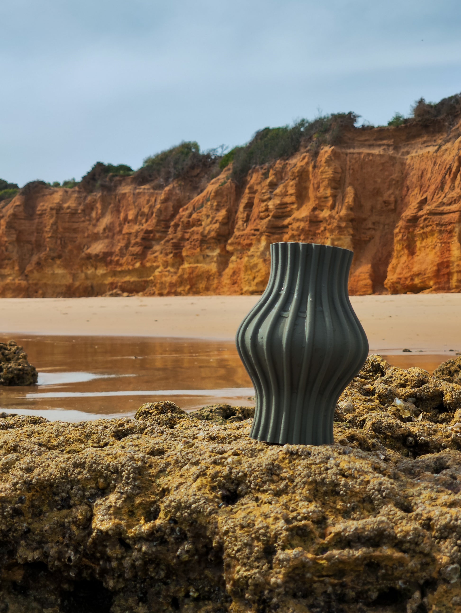 a green vase sitting on top of a rocky beach