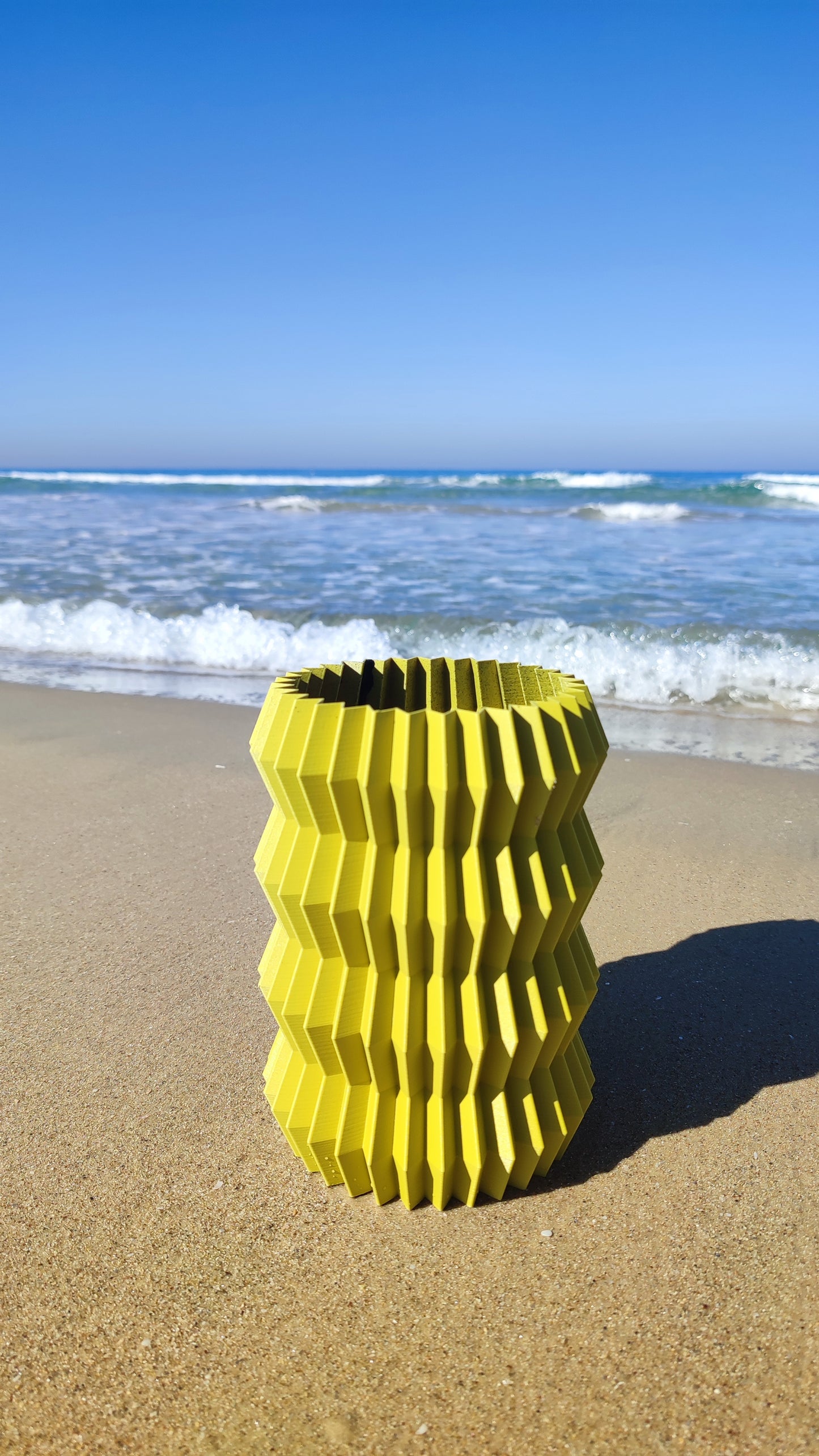 a yellow vase sitting on top of a sandy beach