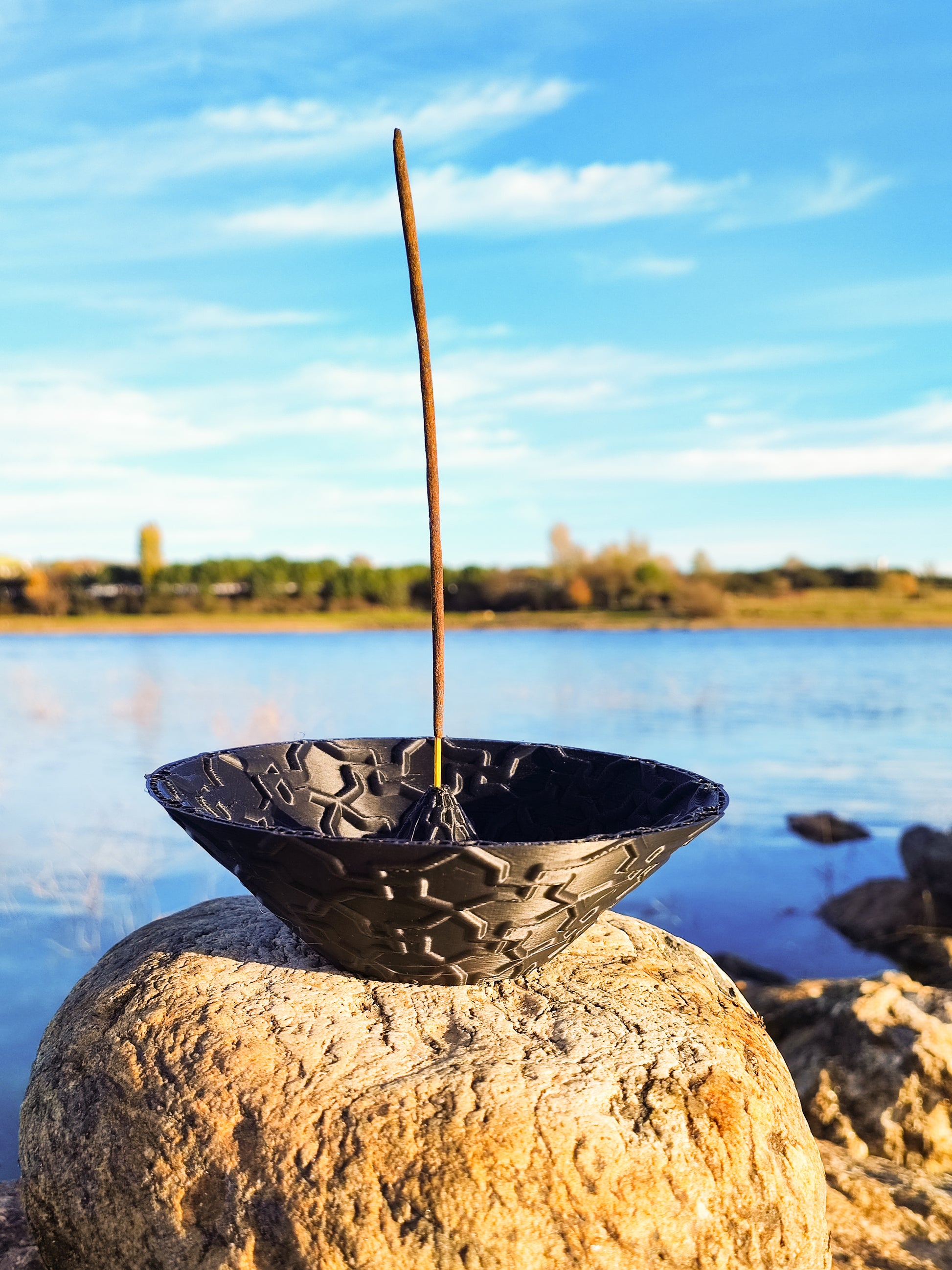 a black bowl sitting on top of a rock next to a body of water